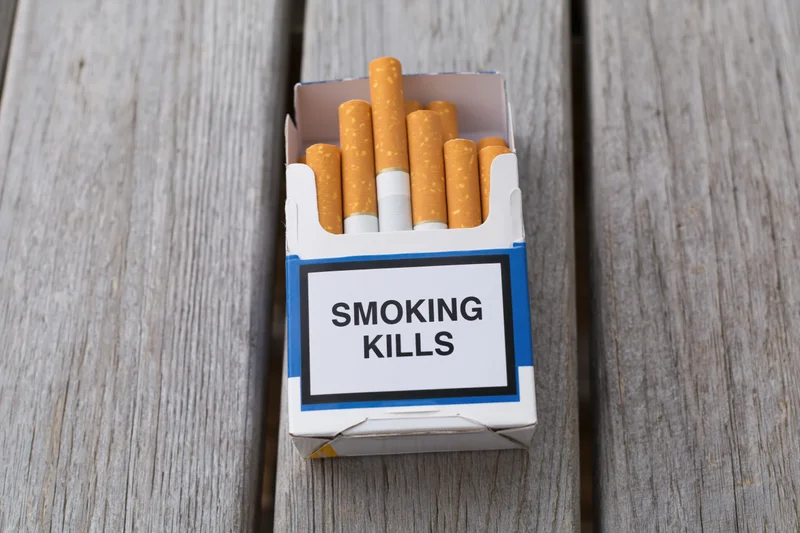 Open cigarette pack with smoking kills warning label on wooden surface