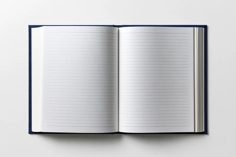 Open hardcover notebook with navy blue cloth binding lying flat on white surface showing blank lined pages