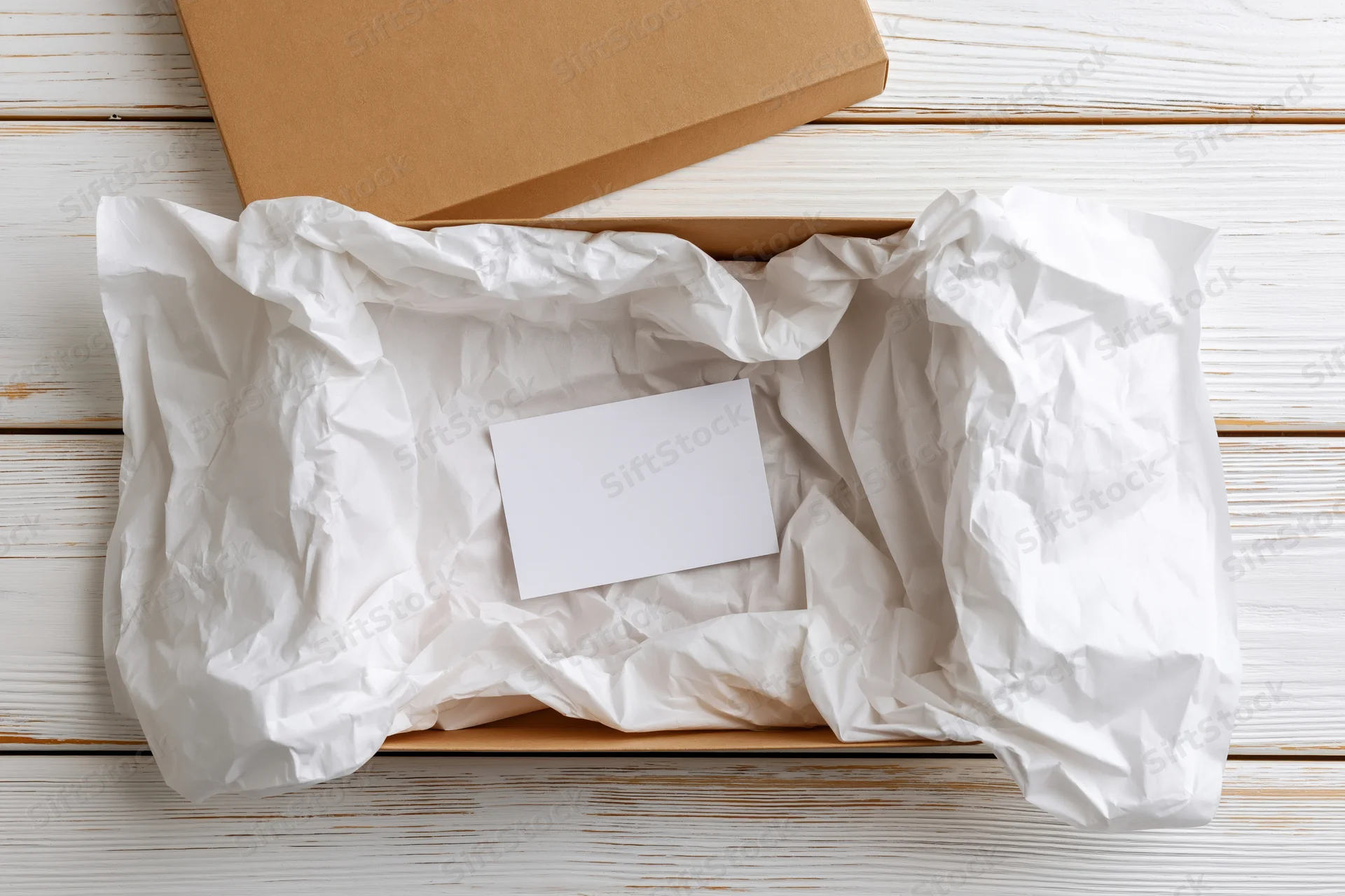 Open kraft cardboard box lined with white tissue paper containing a blank card on a wooden surface