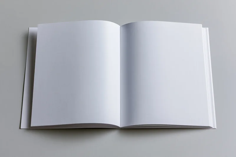 Open square-format booklet lying flat with blank white pages on a gray surface
