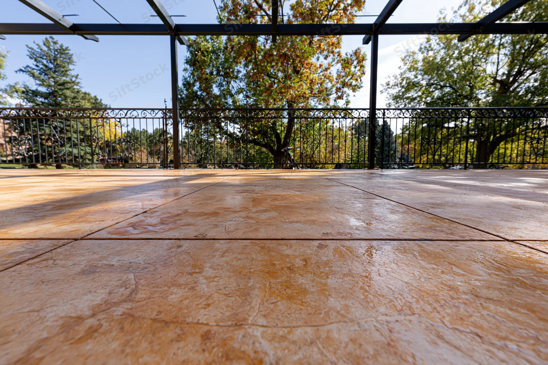 Stamped concrete patio flooring under a pergola with metal railing and autumn trees in the background