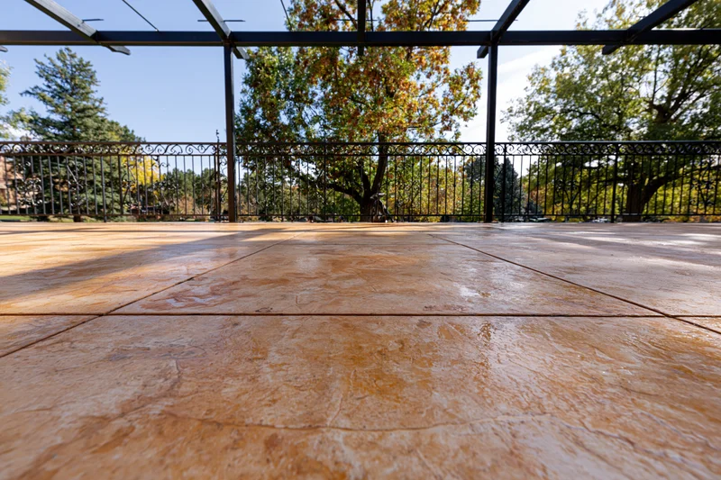 Stamped concrete patio flooring under a pergola with metal railing and autumn trees in the background
