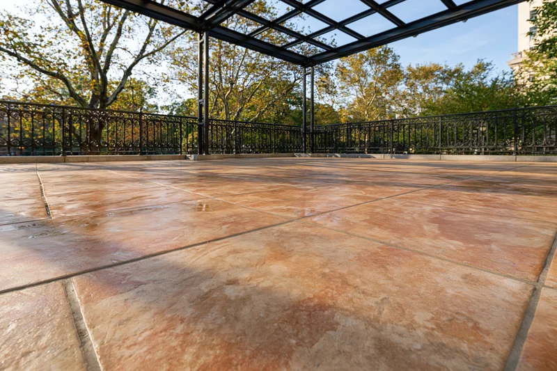 Stamped concrete patio with metal railing and canopy under autumn trees