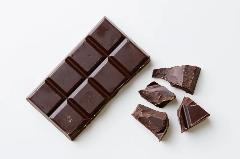 Dark chocolate bar partially broken with pieces on white background