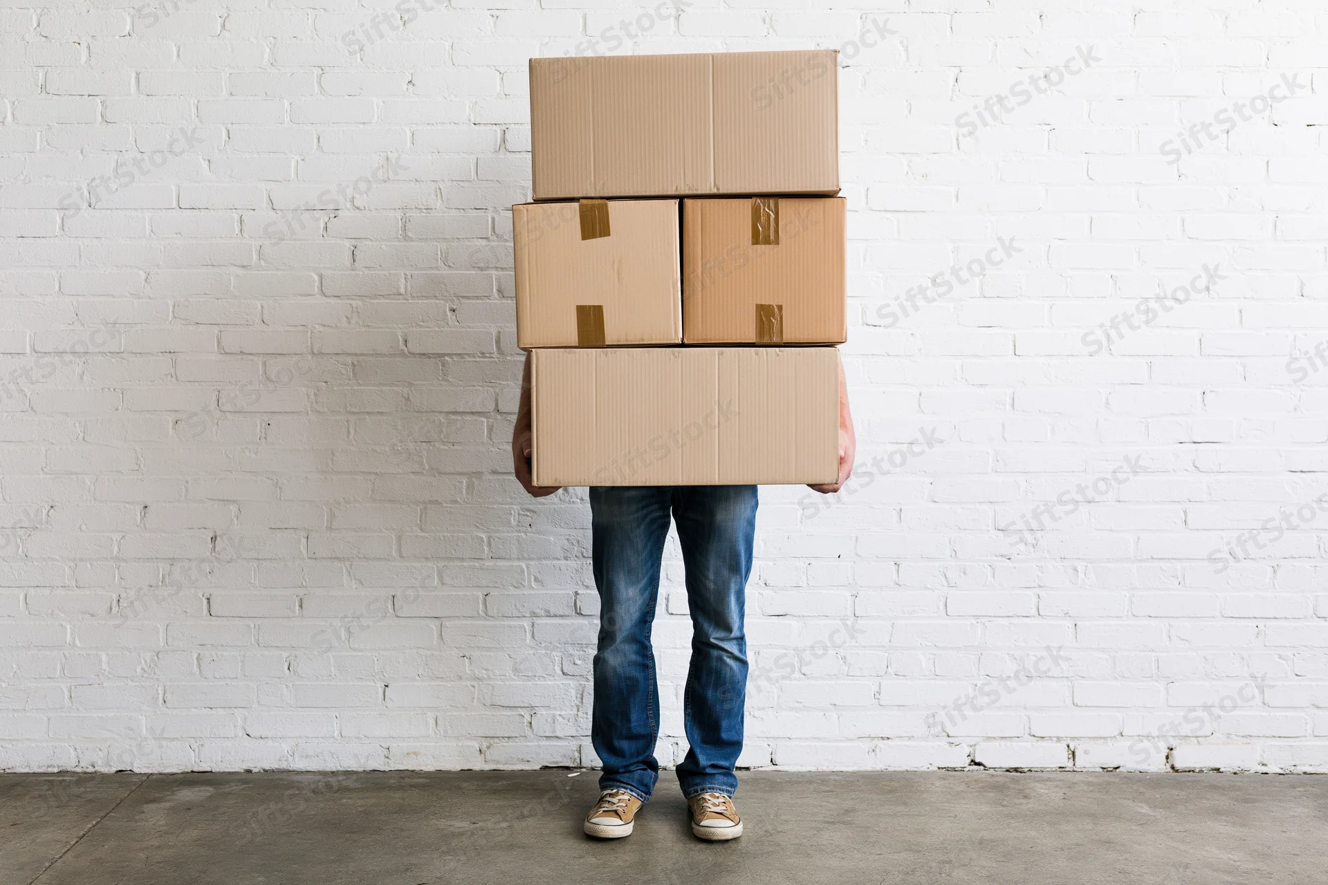 Man carrying stack of cardboard boxes against white brick wall