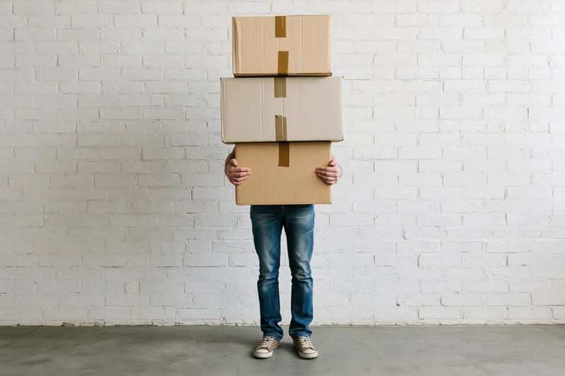 Man holding stack of cardboard boxes against white brick wall
