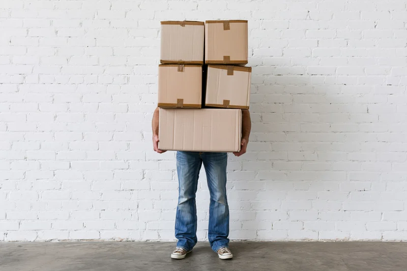 Man carrying stack of cardboard boxes against white brick wall