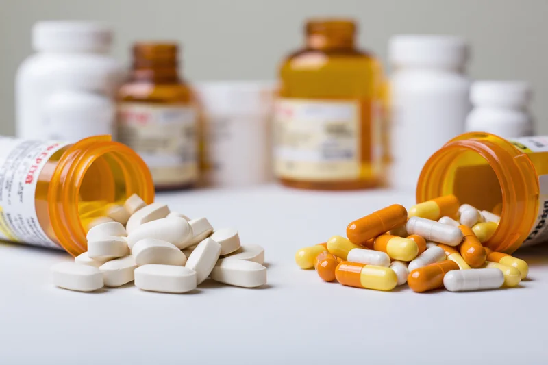 Spilled pills and capsules from orange bottles on a white surface