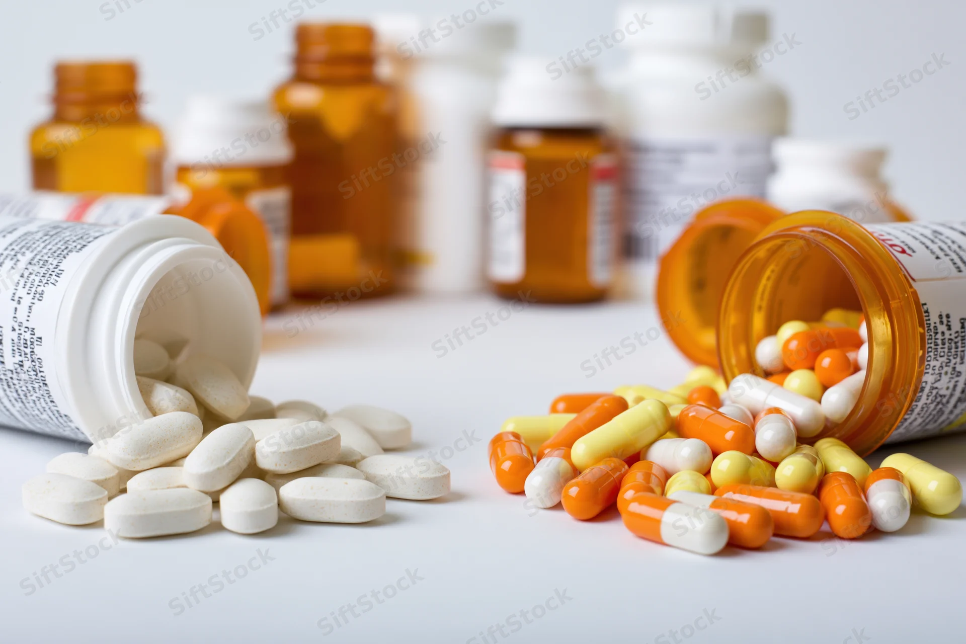 Prescription and supplement pill bottles tipped over on white surface with pills spilled out