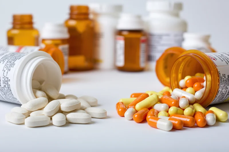 Prescription and supplement pill bottles tipped over on white surface with pills spilled out