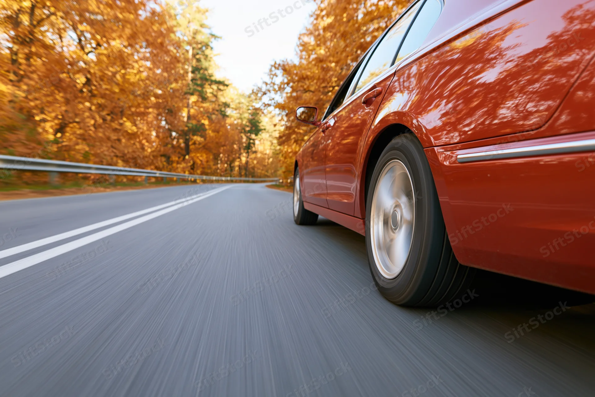 Red-orange sedan driving on a two-lane highway through an autumn forest