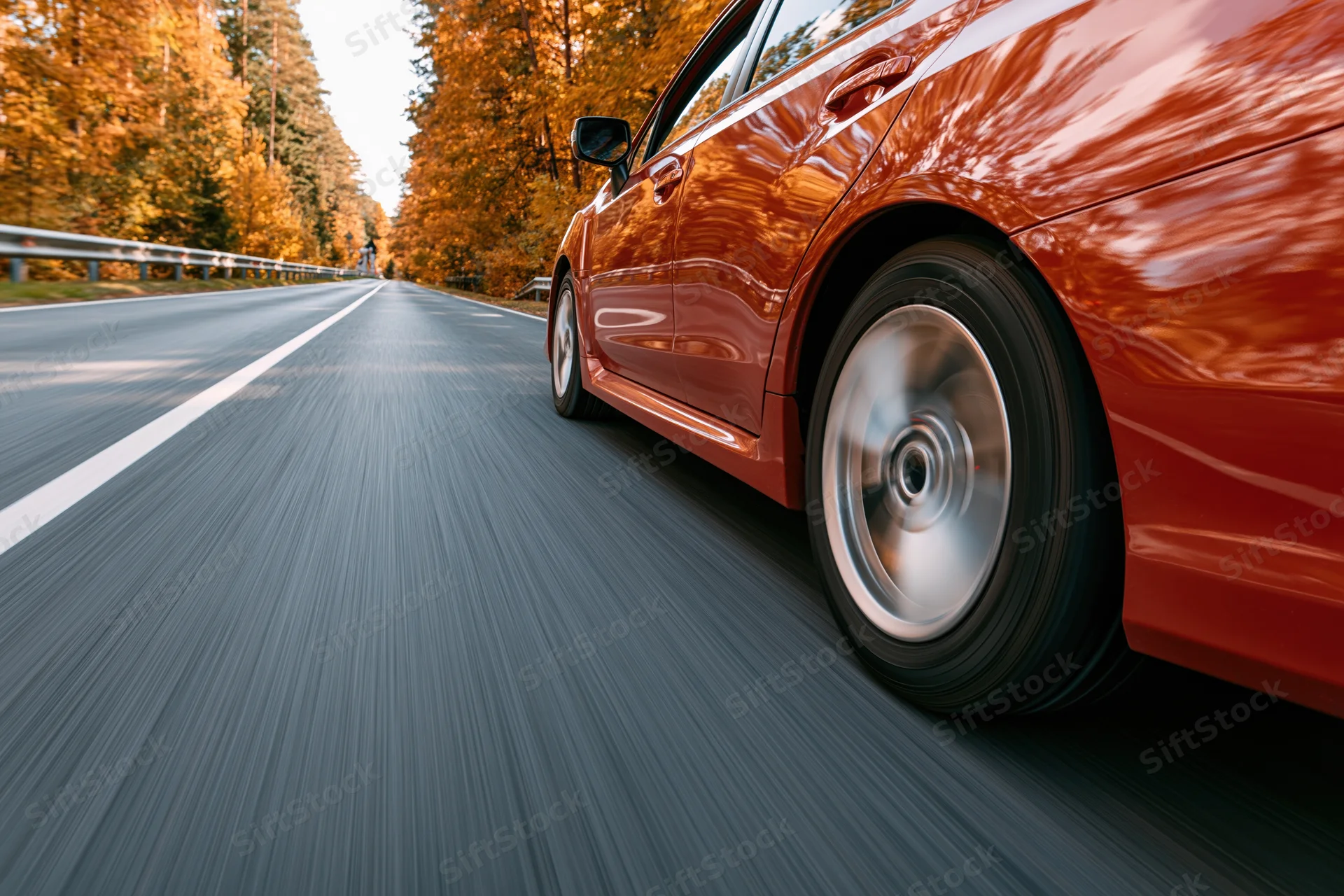 Red-orange sedan driving on a two-lane highway through autumn forest