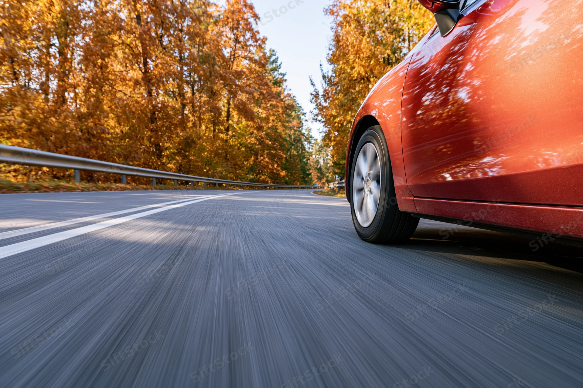 Red-orange sedan driving on a two-lane highway through autumn forest
