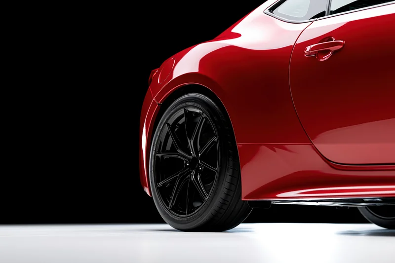 Red sports car side profile showing rear wheel and glossy body on black background