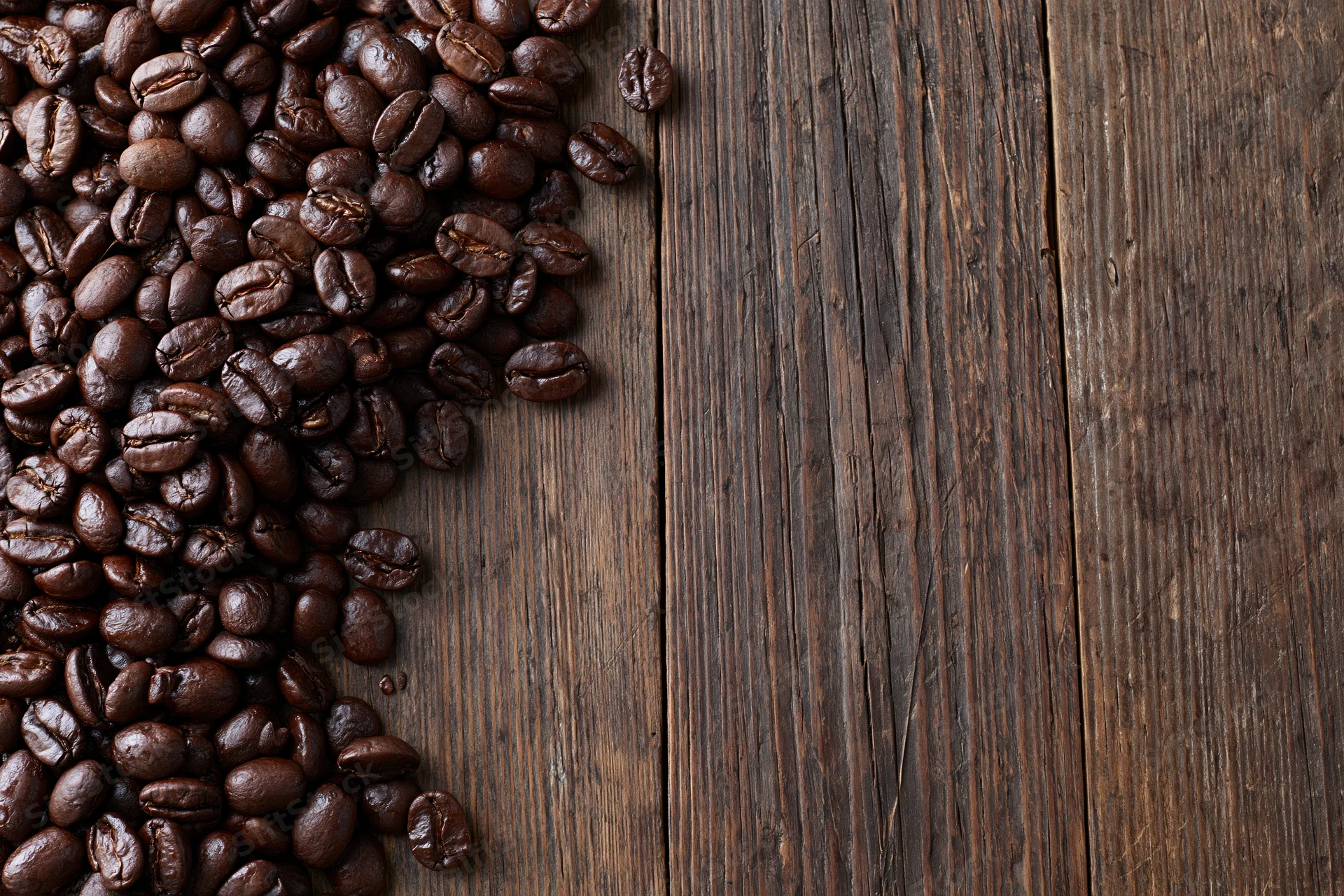 Roasted coffee beans scattered along the left edge of a dark wooden surface