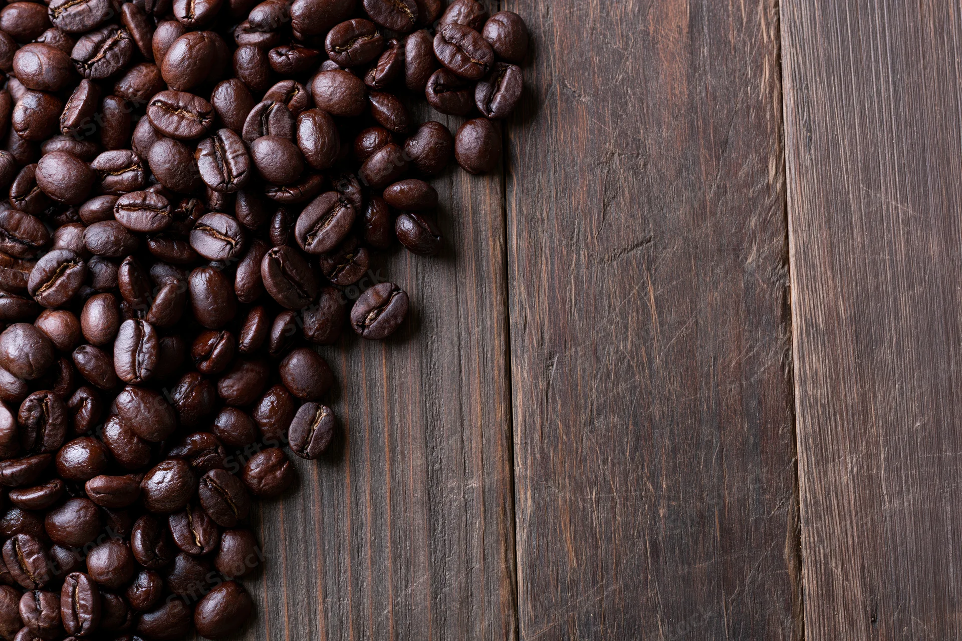 Roasted coffee beans scattered along the left edge of a dark wooden table