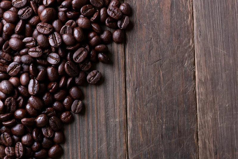 Roasted coffee beans scattered along the left edge of a dark wooden table