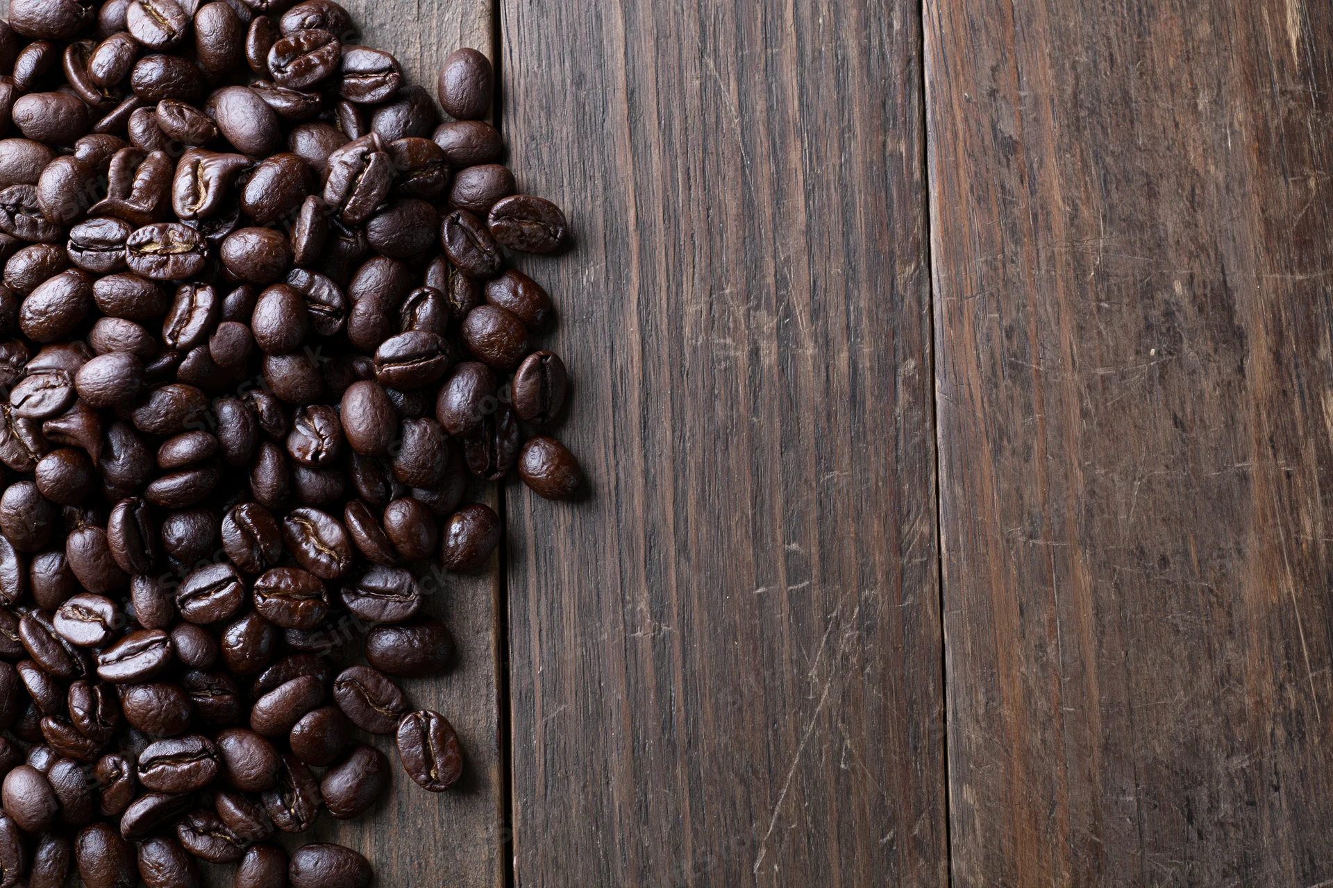 Roasted coffee beans scattered along the left edge of a dark wooden table