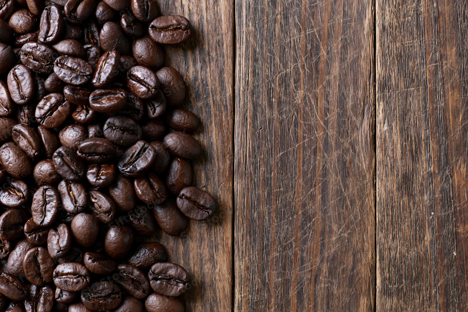 Roasted coffee beans scattered along the left edge of a dark wooden table