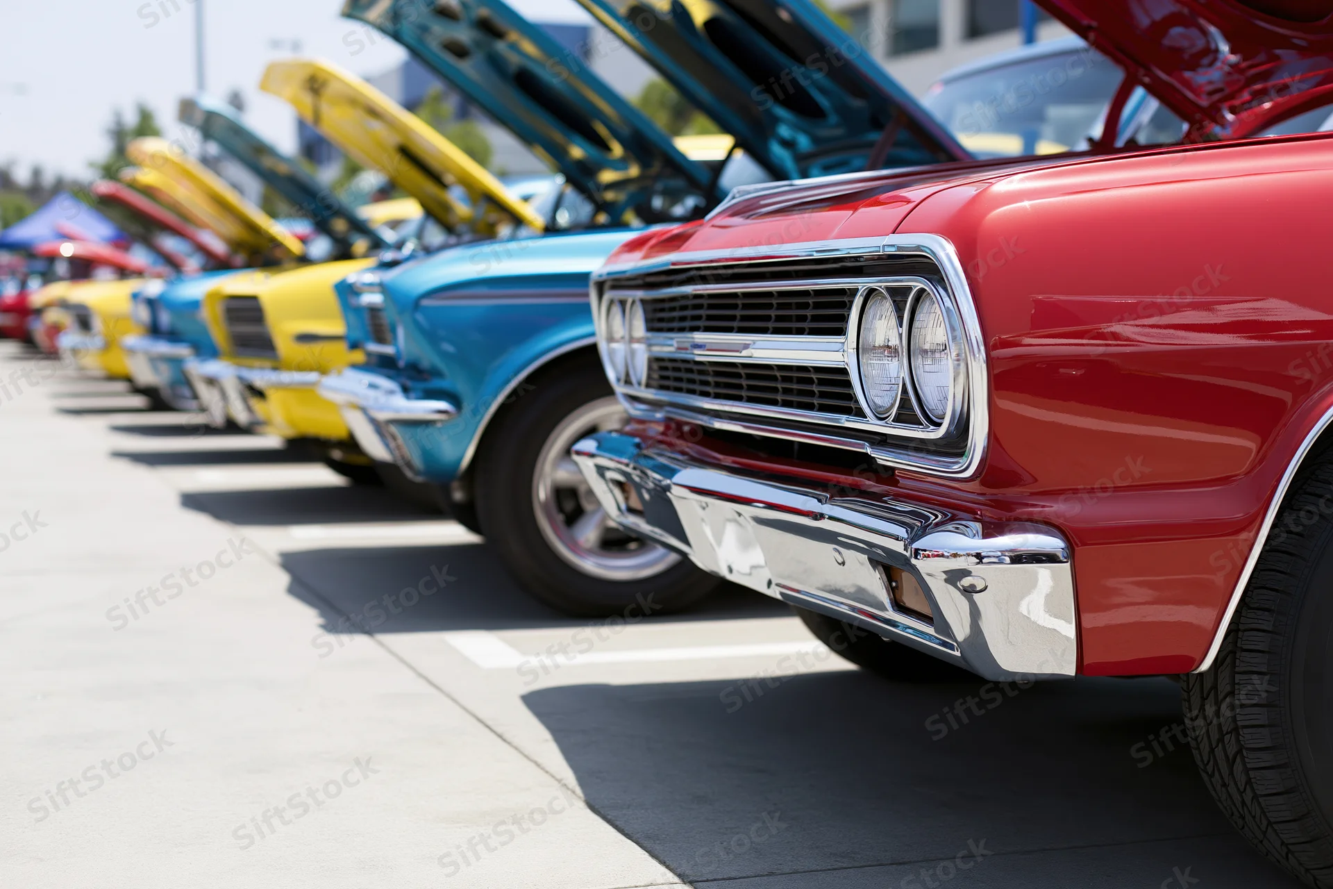 Row of classic american muscle cars with hoods open parked in a line outdoors