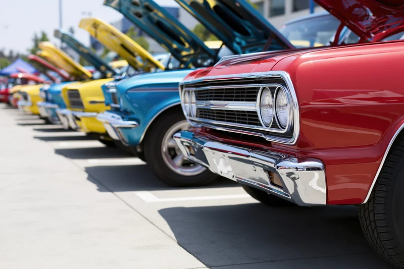 Row of classic american muscle cars with hoods open parked in a line outdoors