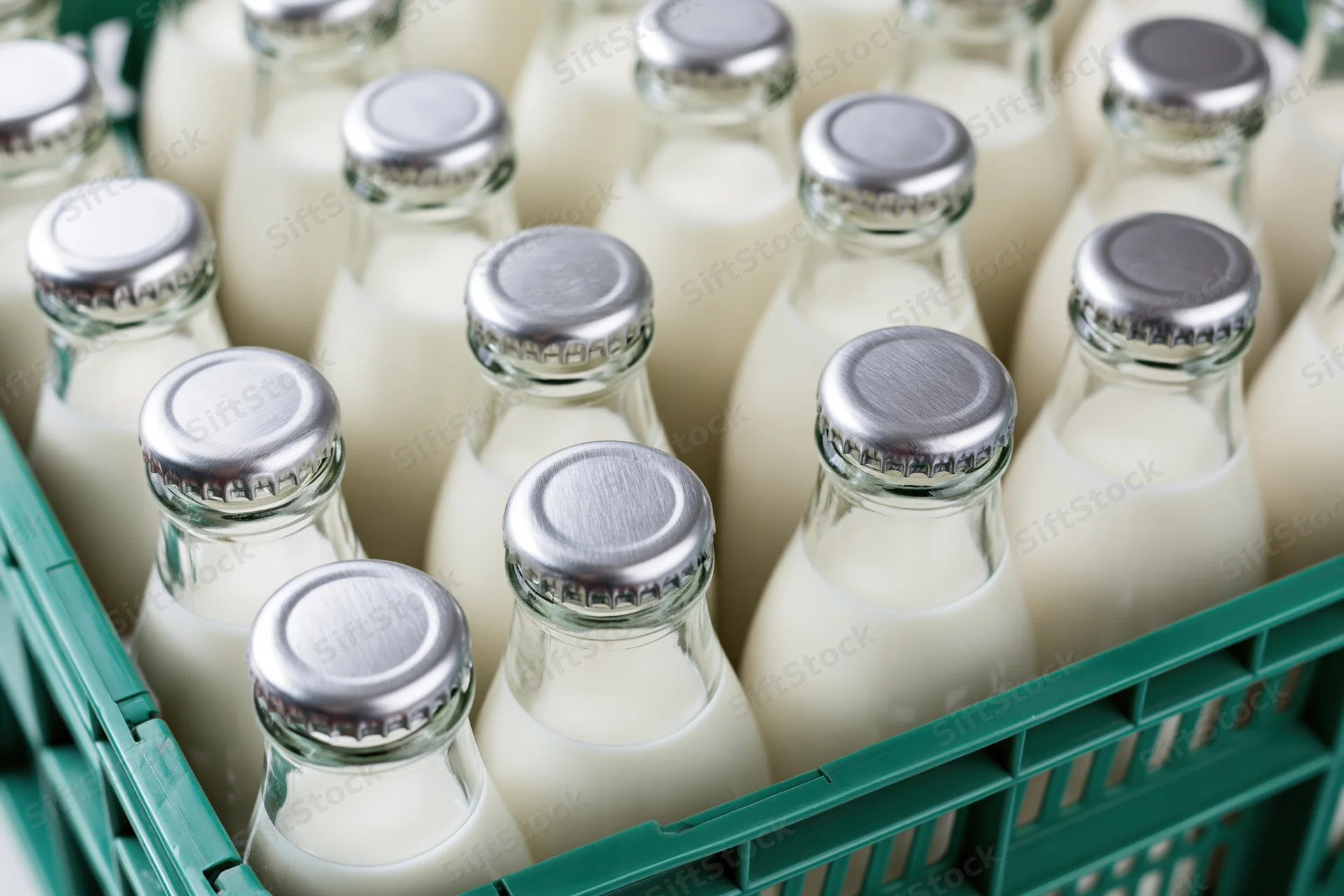 Glass milk bottles with silver foil caps packed tightly in a green plastic crate