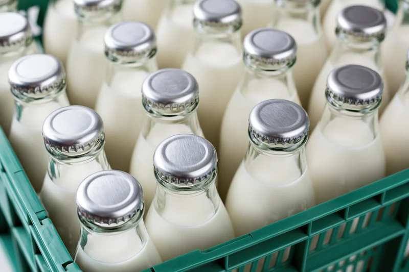 Glass milk bottles with silver foil caps packed tightly in a green plastic crate
