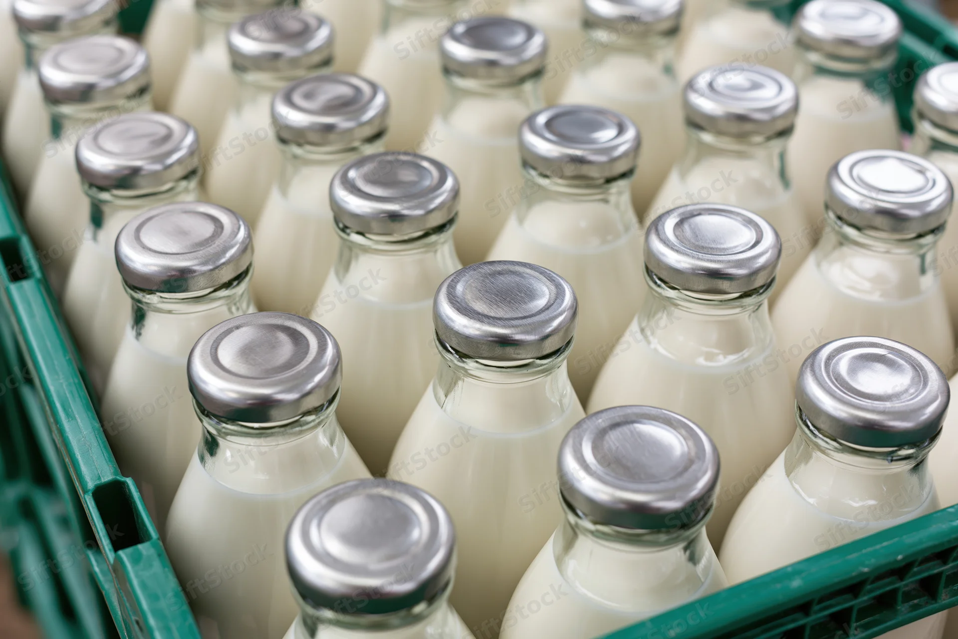 Glass milk bottles with silver foil caps packed tightly in a green plastic crate