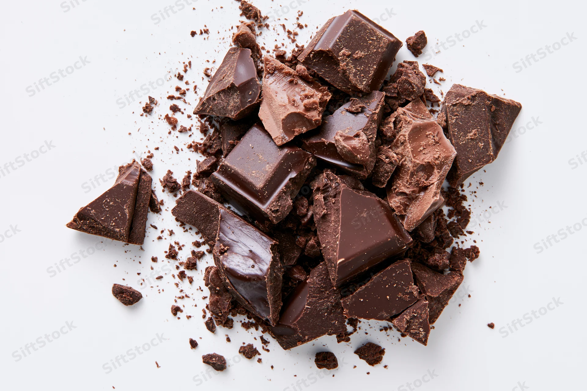 Broken dark chocolate pieces and crumbs scattered on white background