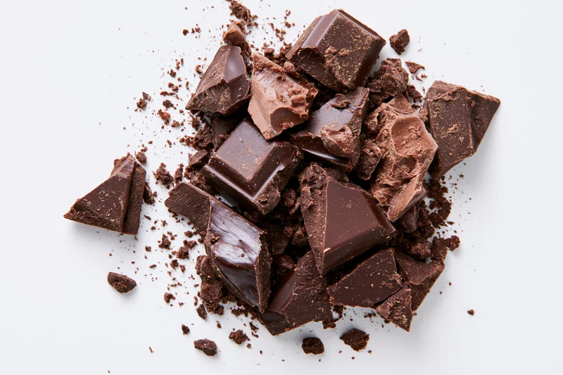 Broken dark chocolate pieces and crumbs scattered on white background