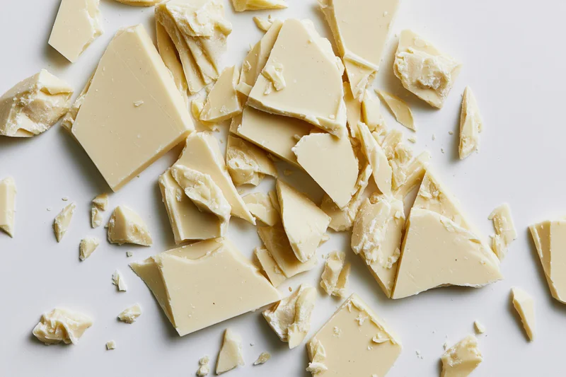 Broken white chocolate pieces scattered on a white surface in a flat lay view