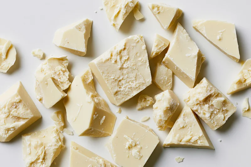 Broken white chocolate pieces scattered on a white surface in a flat lay view