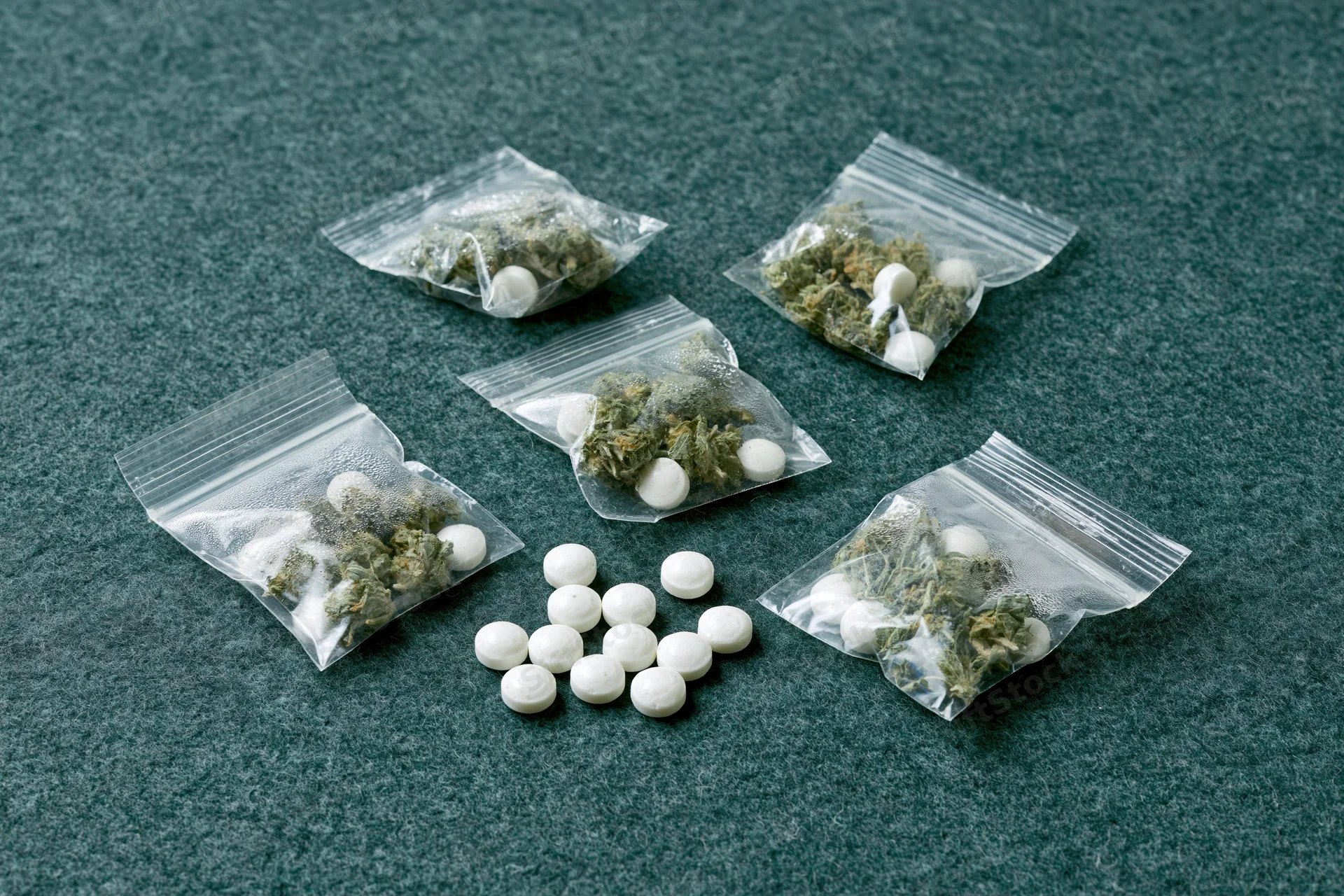 Cannabis buds and white pills in clear zip-lock bags on dark green surface