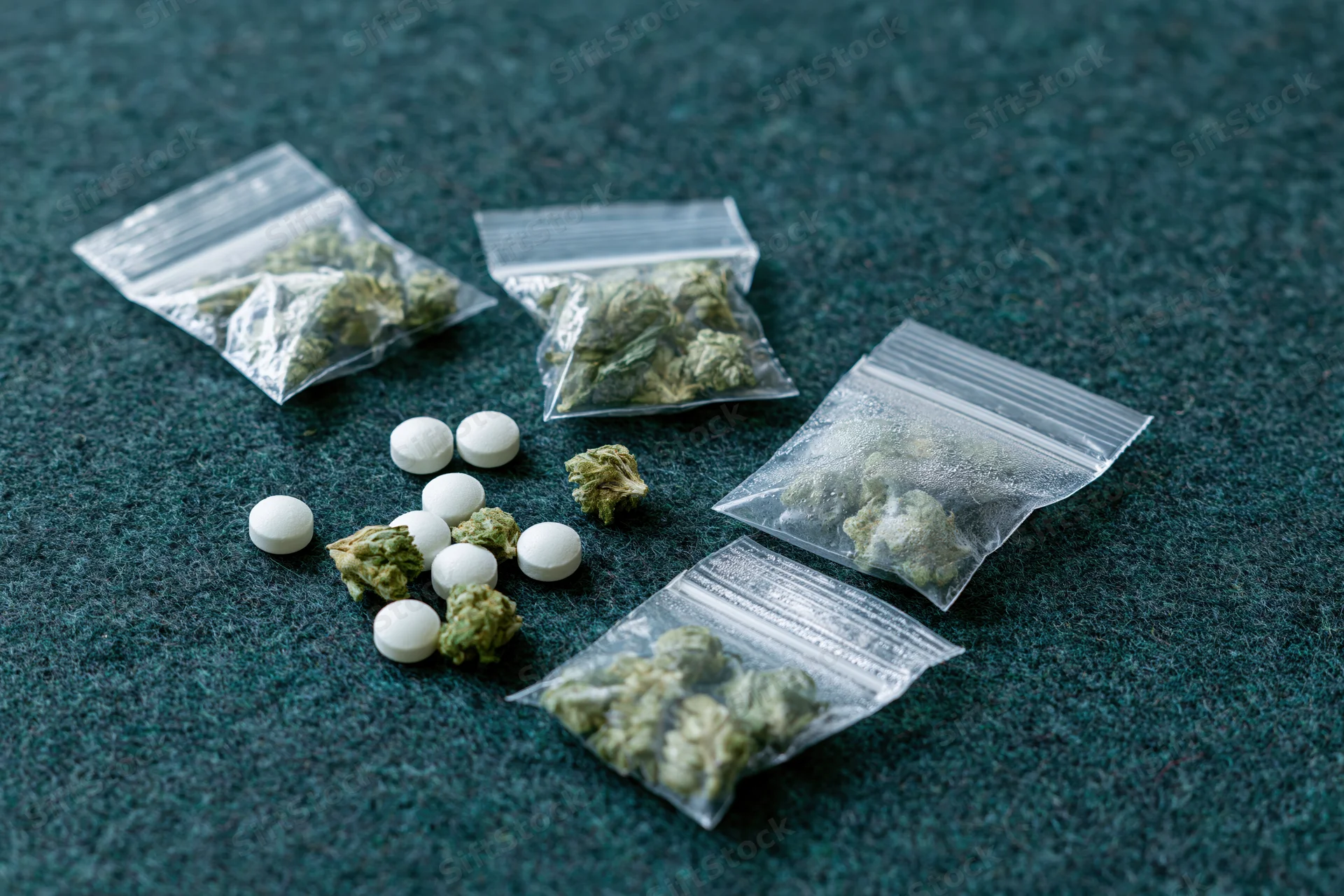 Cannabis buds and white pills in small plastic bags on dark textured surface