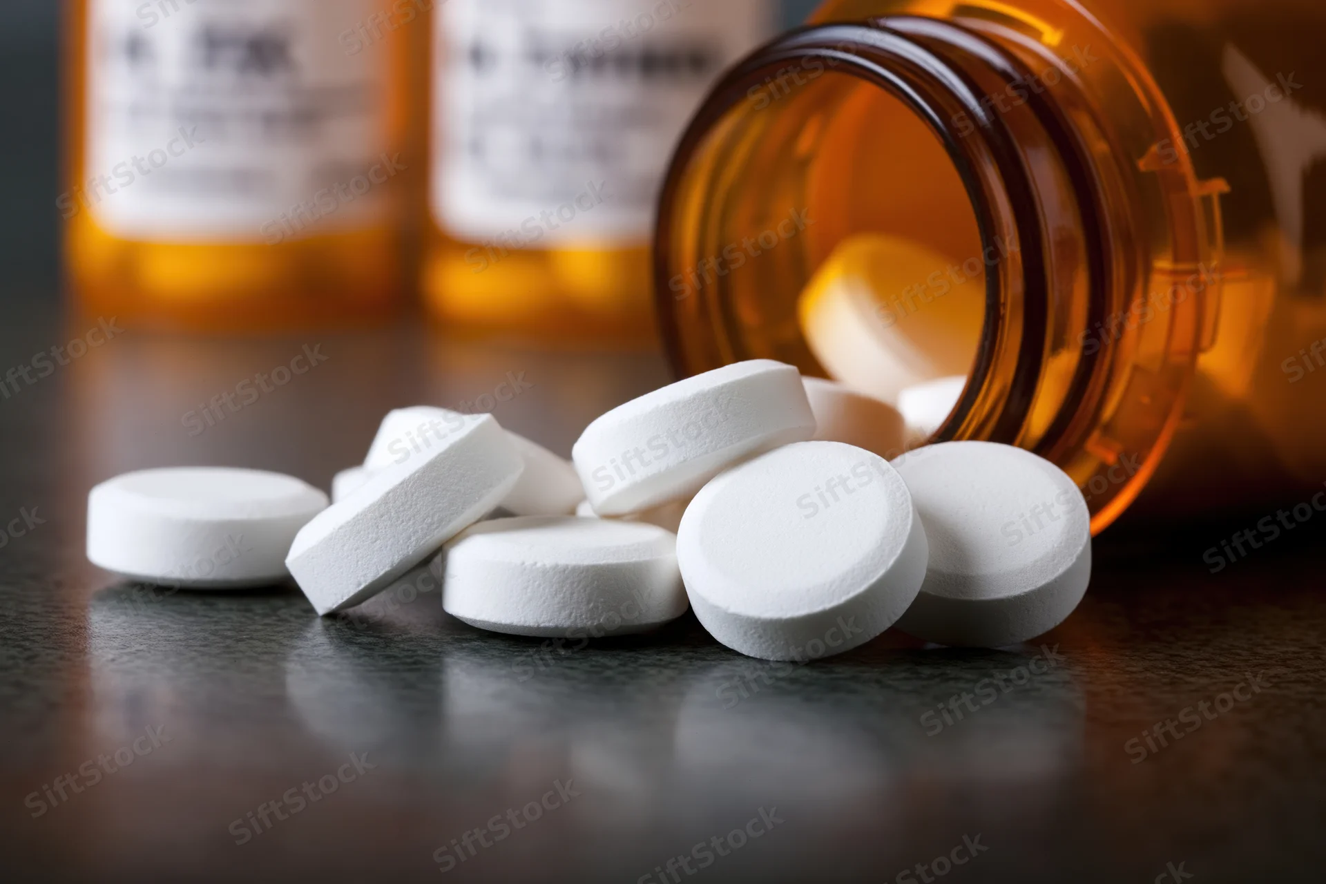White round prescription pills spilled from an amber glass bottle onto a dark surface