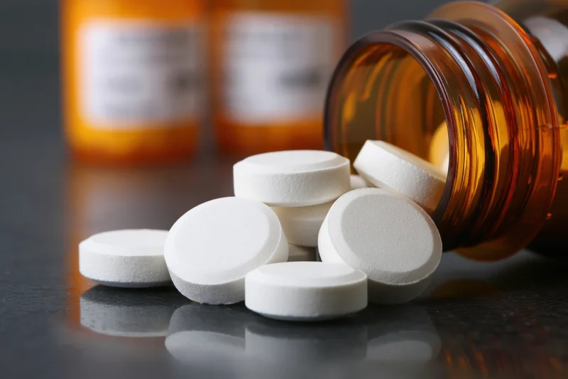 White round prescription pills spilled from an amber bottle on a dark reflective surface