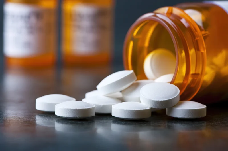 White round pills spilled from an amber prescription bottle onto a dark reflective surface