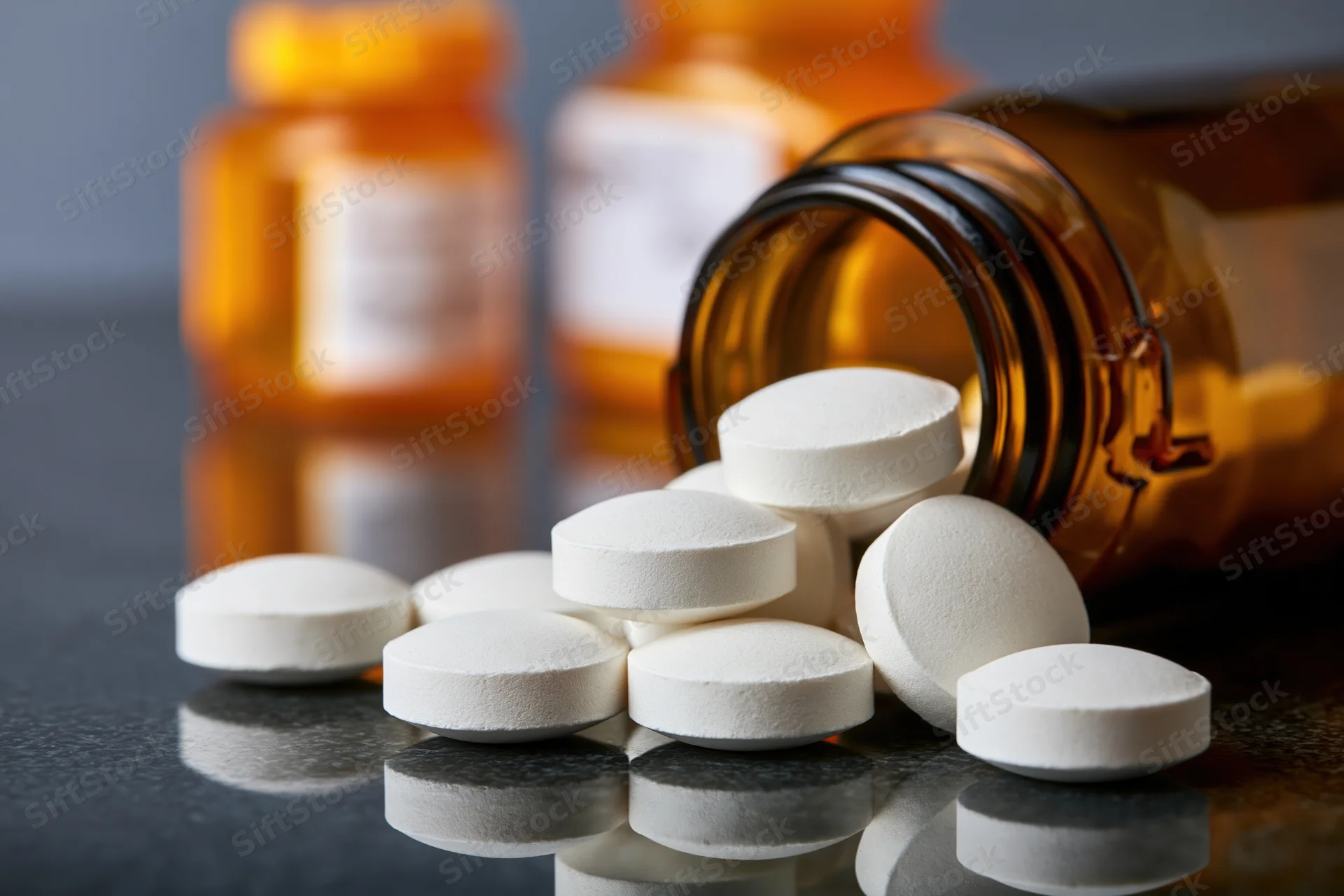 White round pills spilled from an amber glass bottle onto a dark reflective surface