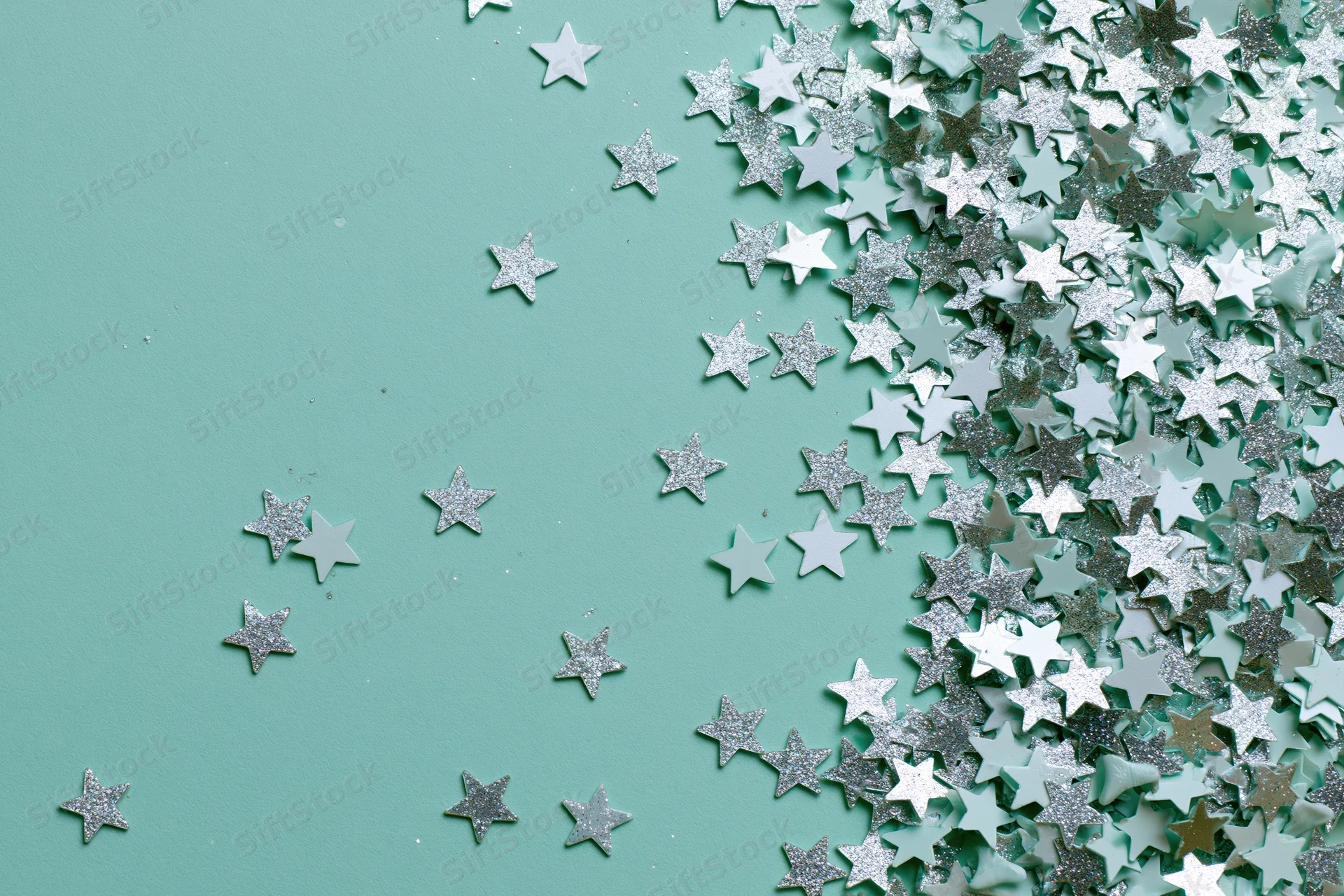 Silver and white star-shaped glitter confetti scattered across a mint green surface with copyspace on the left