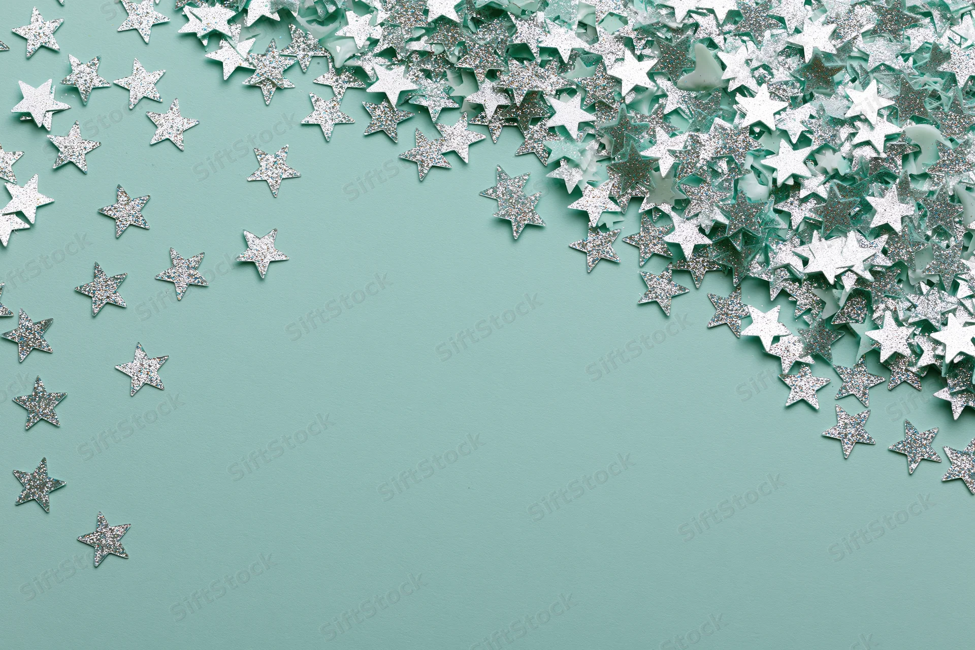 Silver and white star-shaped glitter confetti scattered across a mint green surface with copyspace