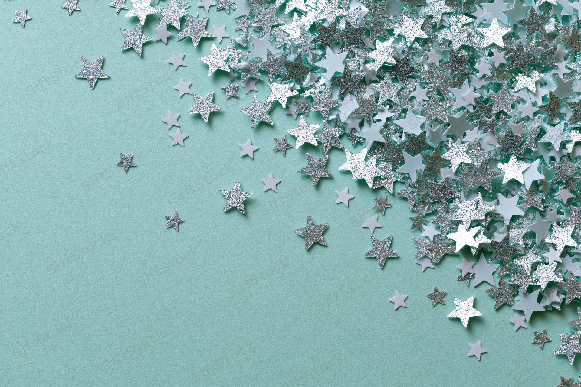 Silver and white star-shaped glitter confetti scattered across a mint green surface with copyspace on the left