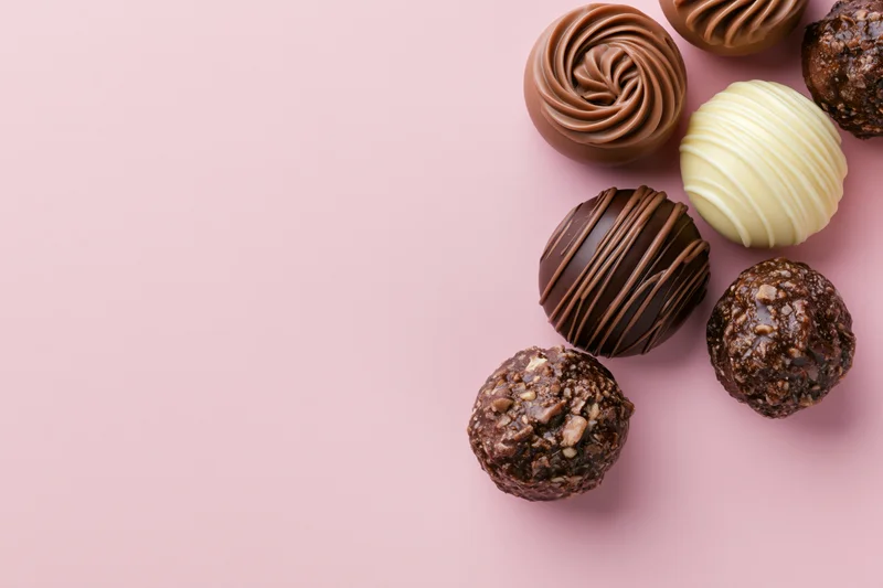 Assorted chocolate pralines and truffles arranged loosely on pink background with copyspace