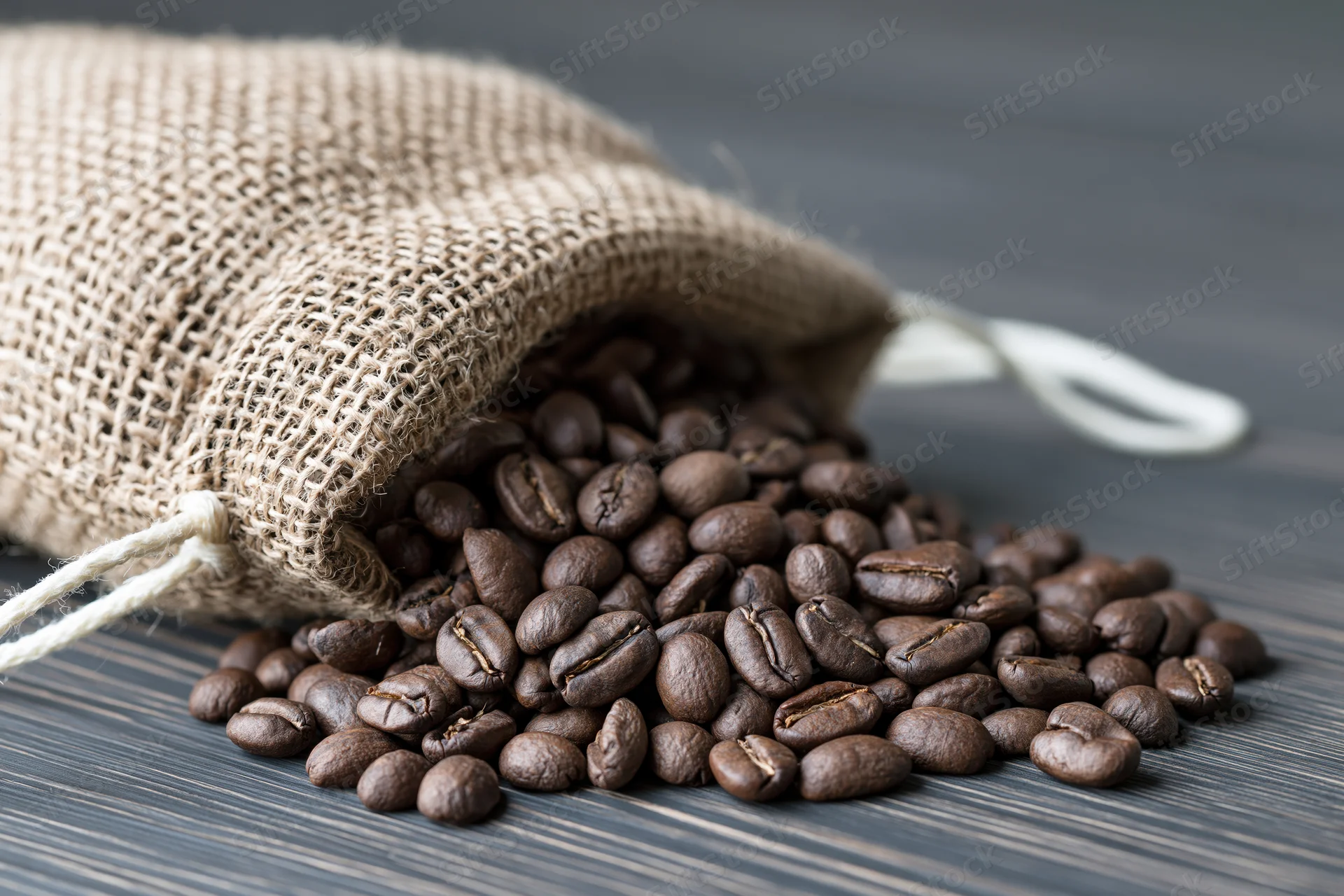 Roasted coffee beans spilling from a burlap sack onto a dark wooden surface