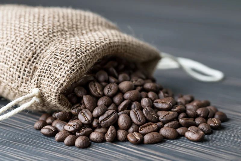 Roasted coffee beans spilling from a burlap sack onto a dark wooden surface