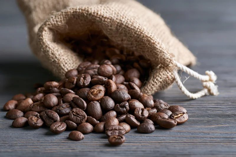 Roasted coffee beans spilling from a burlap sack onto a dark wooden surface