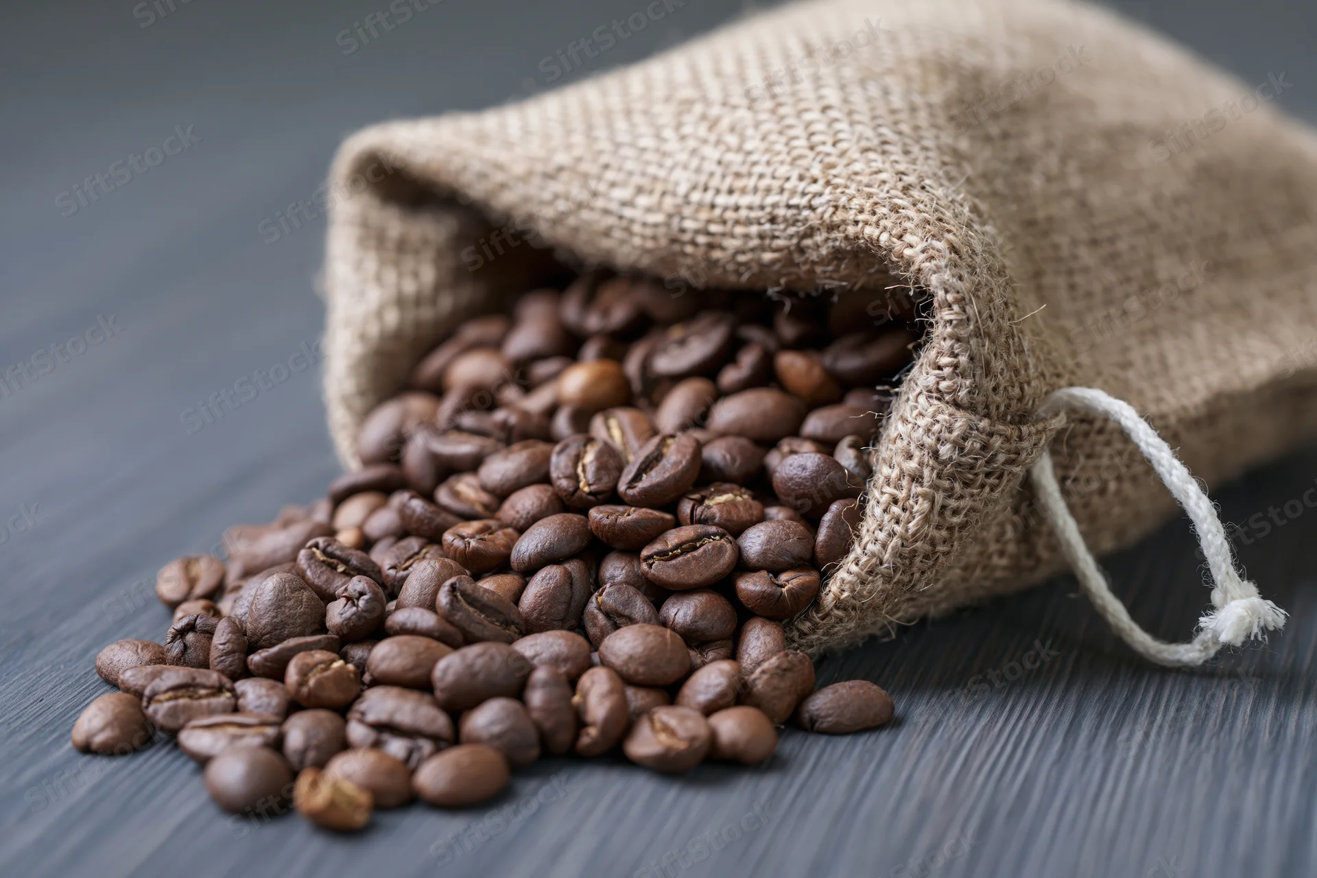 Roasted coffee beans spilling from a burlap sack onto a dark wooden surface