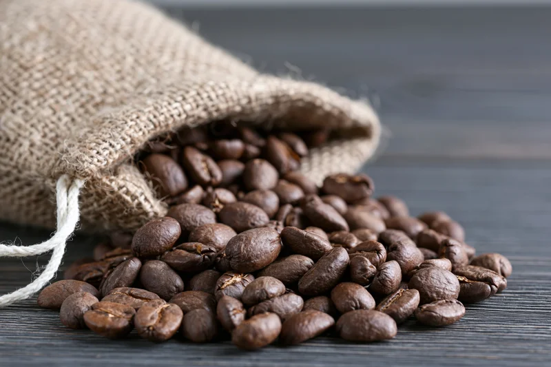 Roasted coffee beans spilling from a burlap sack onto a dark wooden surface