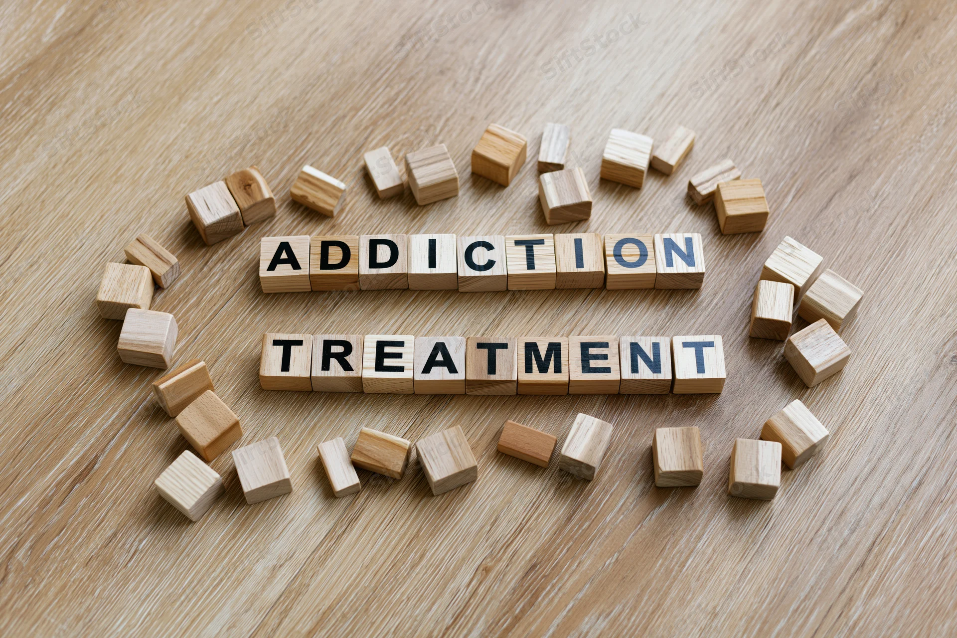 Wooden letter cubes spelling addiction treatment arranged on a light oak surface