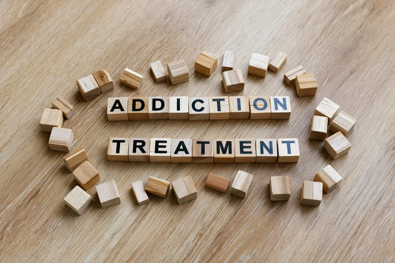 Wooden letter cubes spelling addiction treatment arranged on a light oak surface