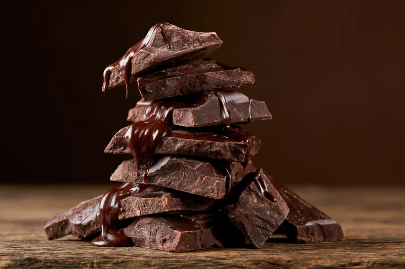 Broken dark chocolate chunks piled unevenly on a wooden surface with melted chocolate dripping down